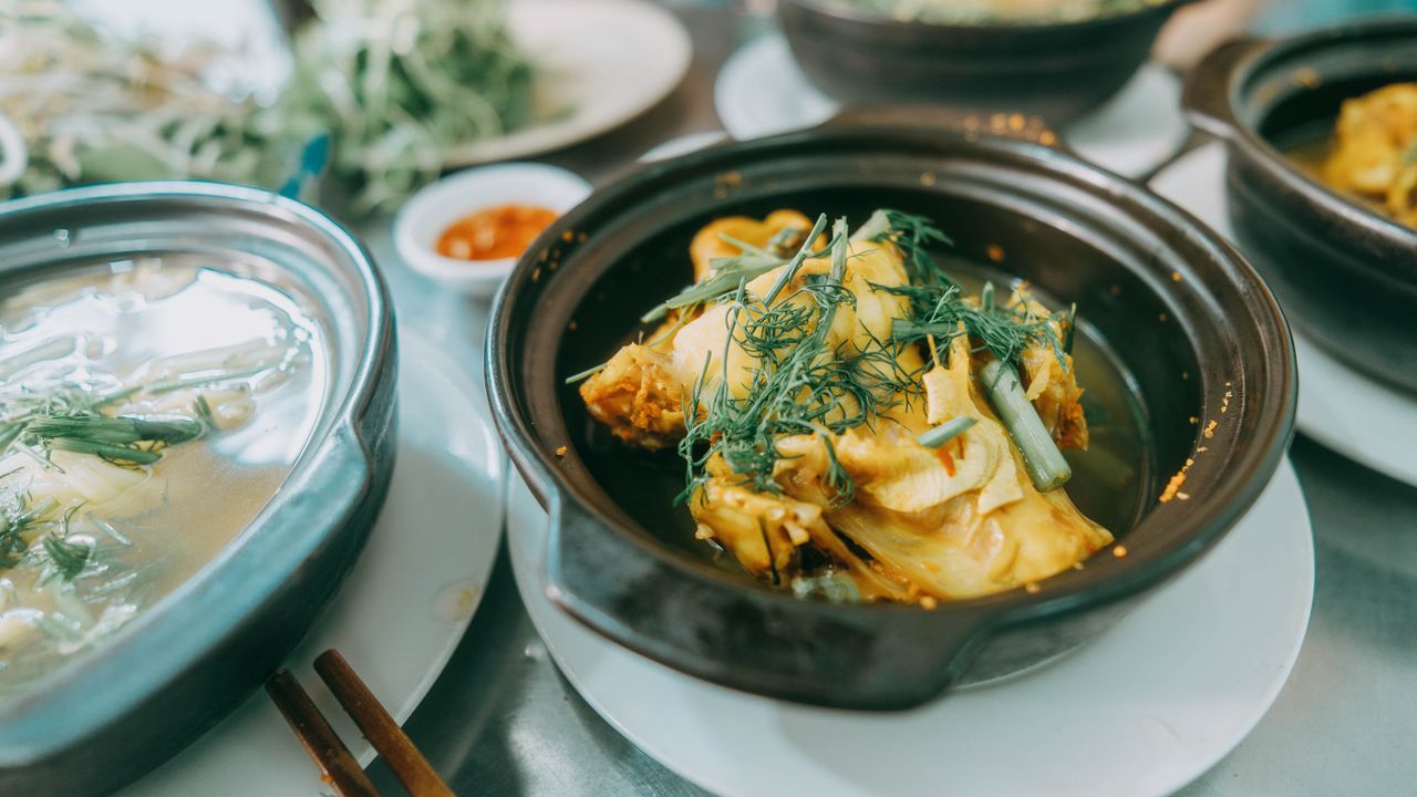A close-up of traditional Vietnamese fish soup with herbs in a clay pot, served fresh.