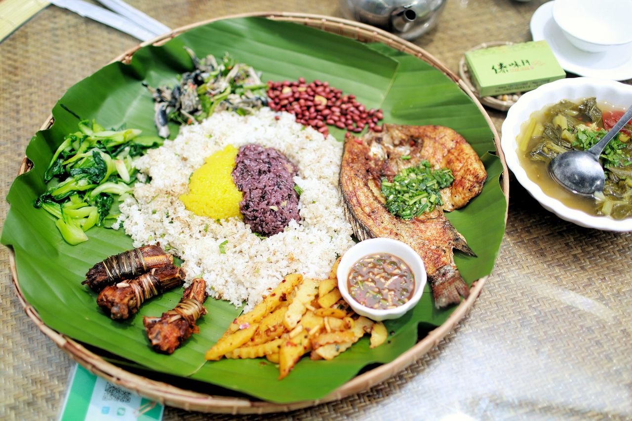 Delicious traditional Yunnan meal served on a banana leaf featuring rice, grilled fish, and vegetables.