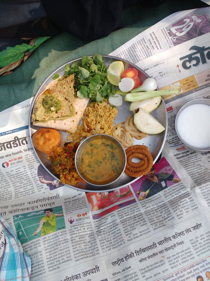 Delicious Indian thali with diverse dishes served on a traditional metal plate over a newspaper.